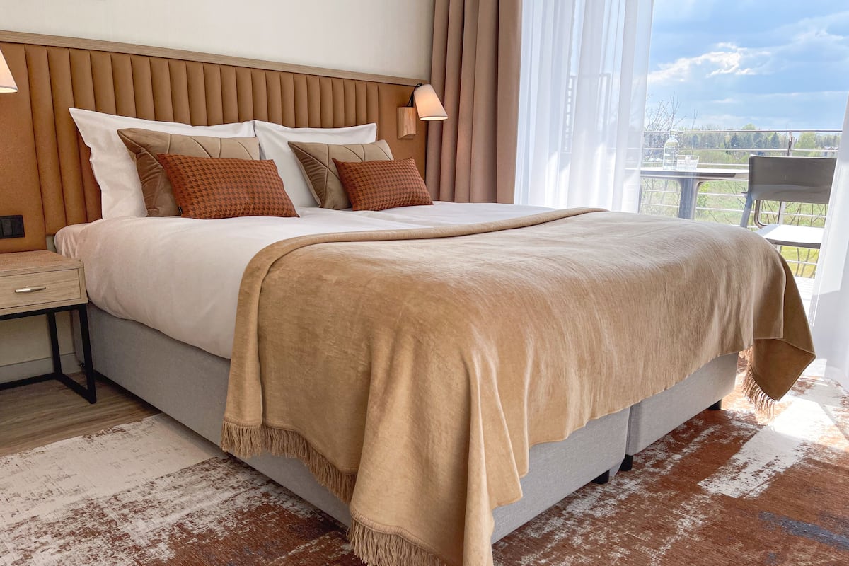 A neatly made bed with a beige blanket and pillows, a wooden headboard, and a bedside table with a lamp.