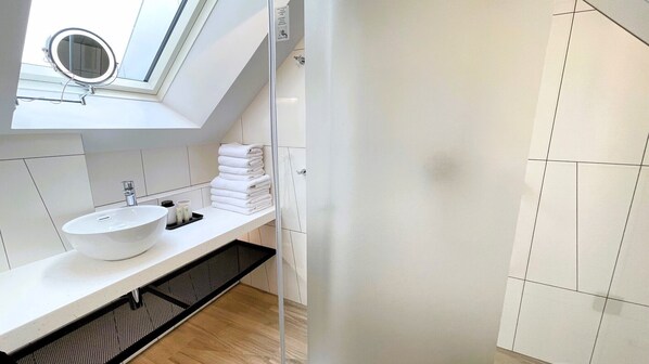 A modern bathroom with a skylight, a white sink, and neatly stacked towels.