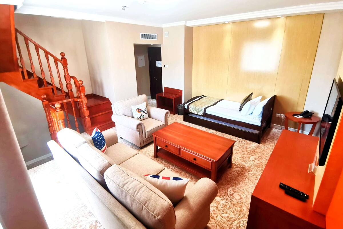 Ein Hotelzimmer mit Bett, einer Couch, einem Holztisch, einem Fernseher und einem kleinen Tisch mit Fernbedienung.