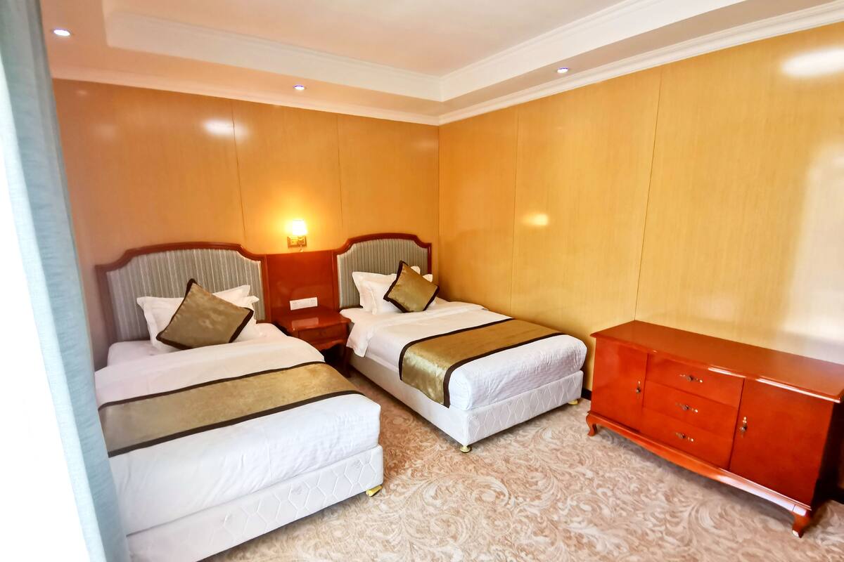 Ein Hotelzimmer mit zwei Betten, einem Holzschrank und einem Nachttisch mit Lampe.