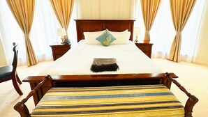 A large bed with a wooden headboard, two bedside tables with lamps, and a striped bench. - Bayangol Hotel & Resort (Ulaanbaatar)