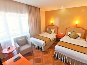 A hotel room with two beds, a small table with a remote control, a chair, and a window with curtains. - Bayangol Hotel & Resort (Ulaanbaatar)