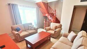 A living room with a sofa, armchair, and coffee table. A staircase with a wooden railing is visible in the background. - Bayangol Hotel & Resort (Ulaanbaatar)