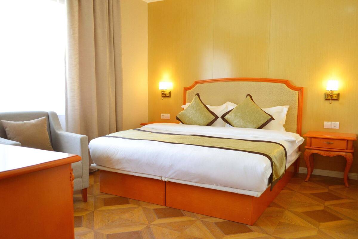 Ein Hotelzimmer mit Bett, Sessel, Nachttisch und Lampe.