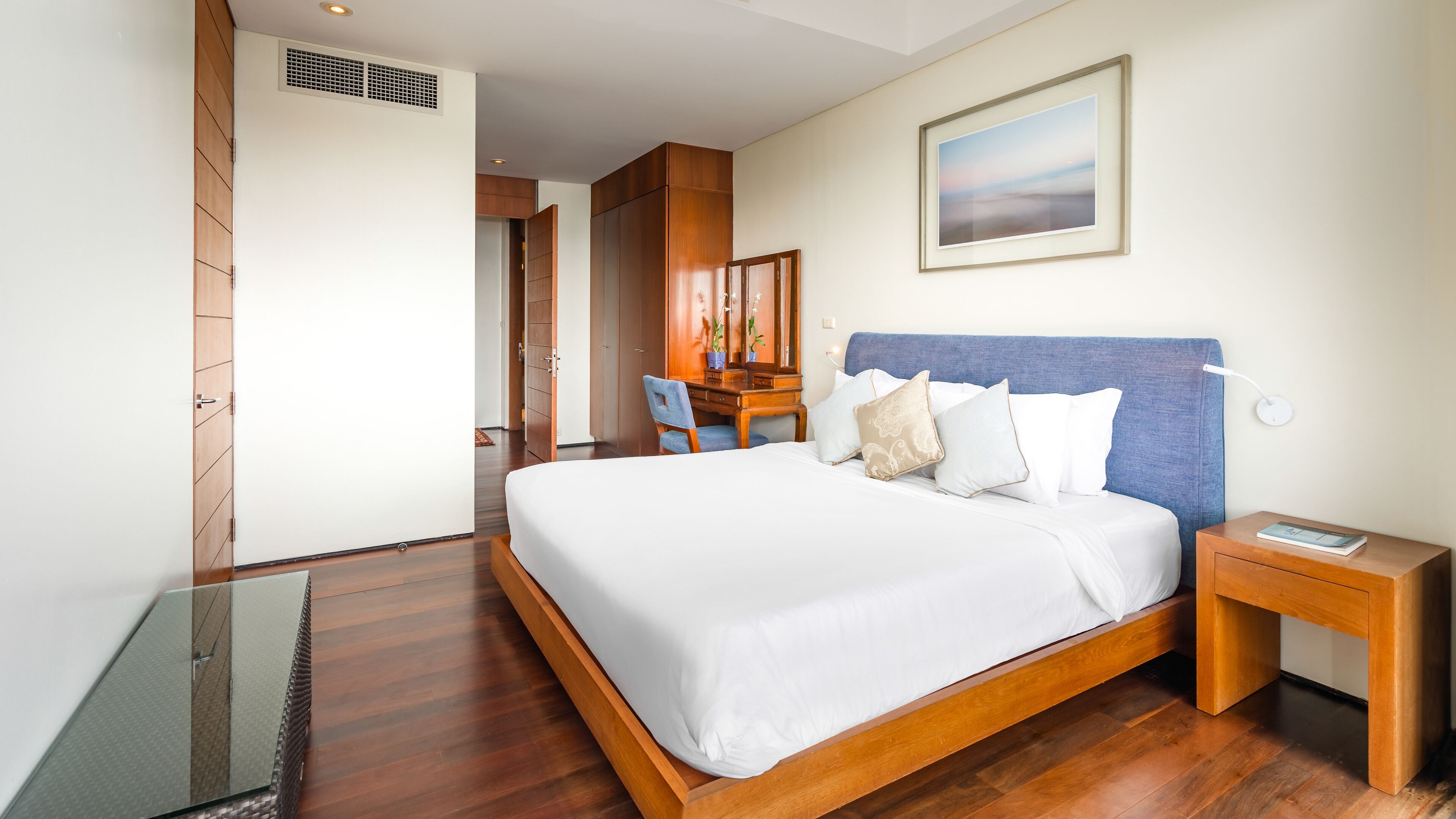 A modern hotel room with a large bed, wooden headboard, and a desk with a chair.