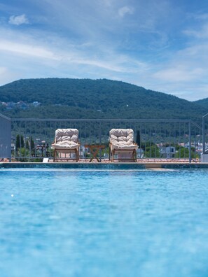 A pool with two lounge chairs facing the water, surrounded by a metal fence, with a mountainous backdrop. - Ma-Si Urla Hotel (Urla)
