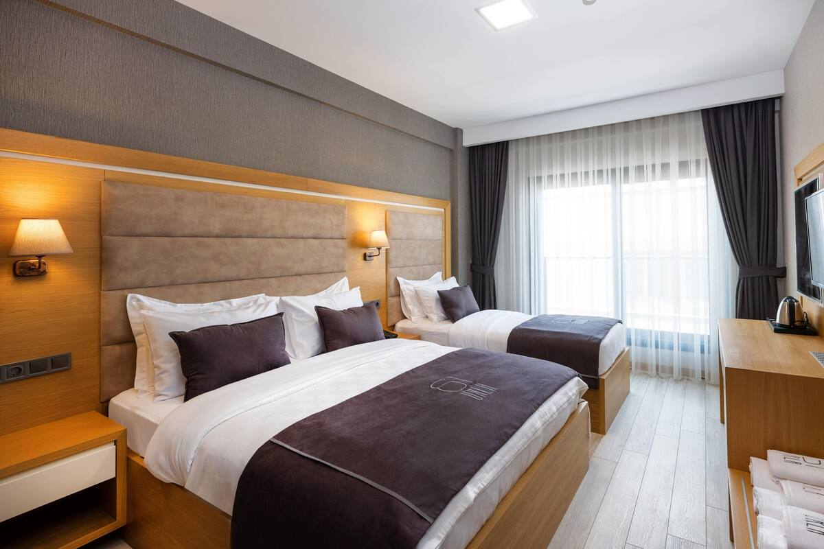 A hotel room with two beds, a desk, a TV, and a window with curtains.
