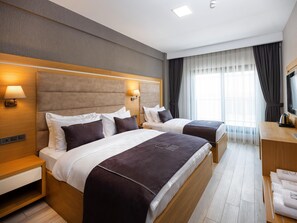 A hotel room with two beds, a desk, a TV, and a window with curtains. - Ma-Si Urla Hotel (Urla)