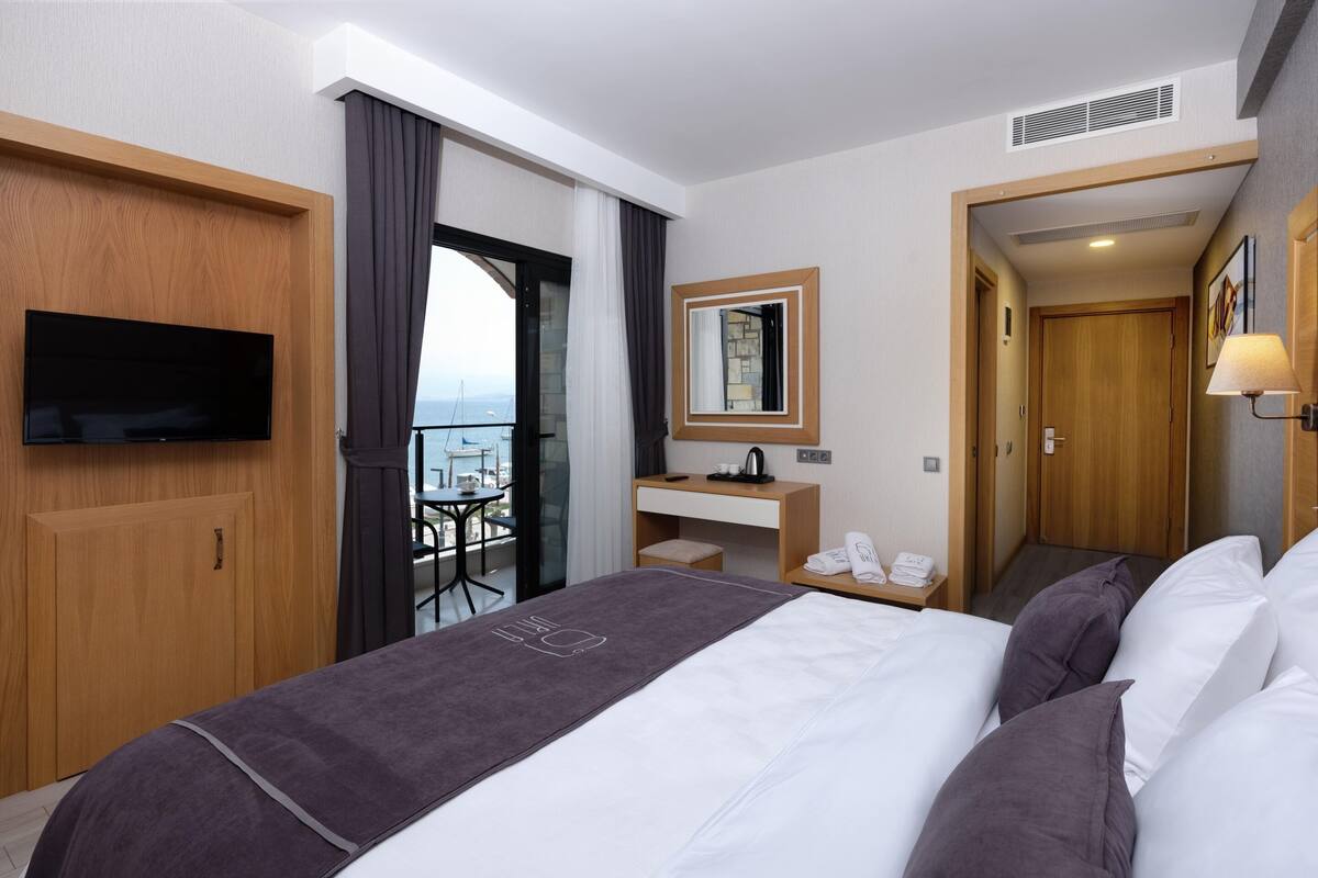 A hotel room with a bed, a desk with a mirror, a TV, and a balcony with a view.