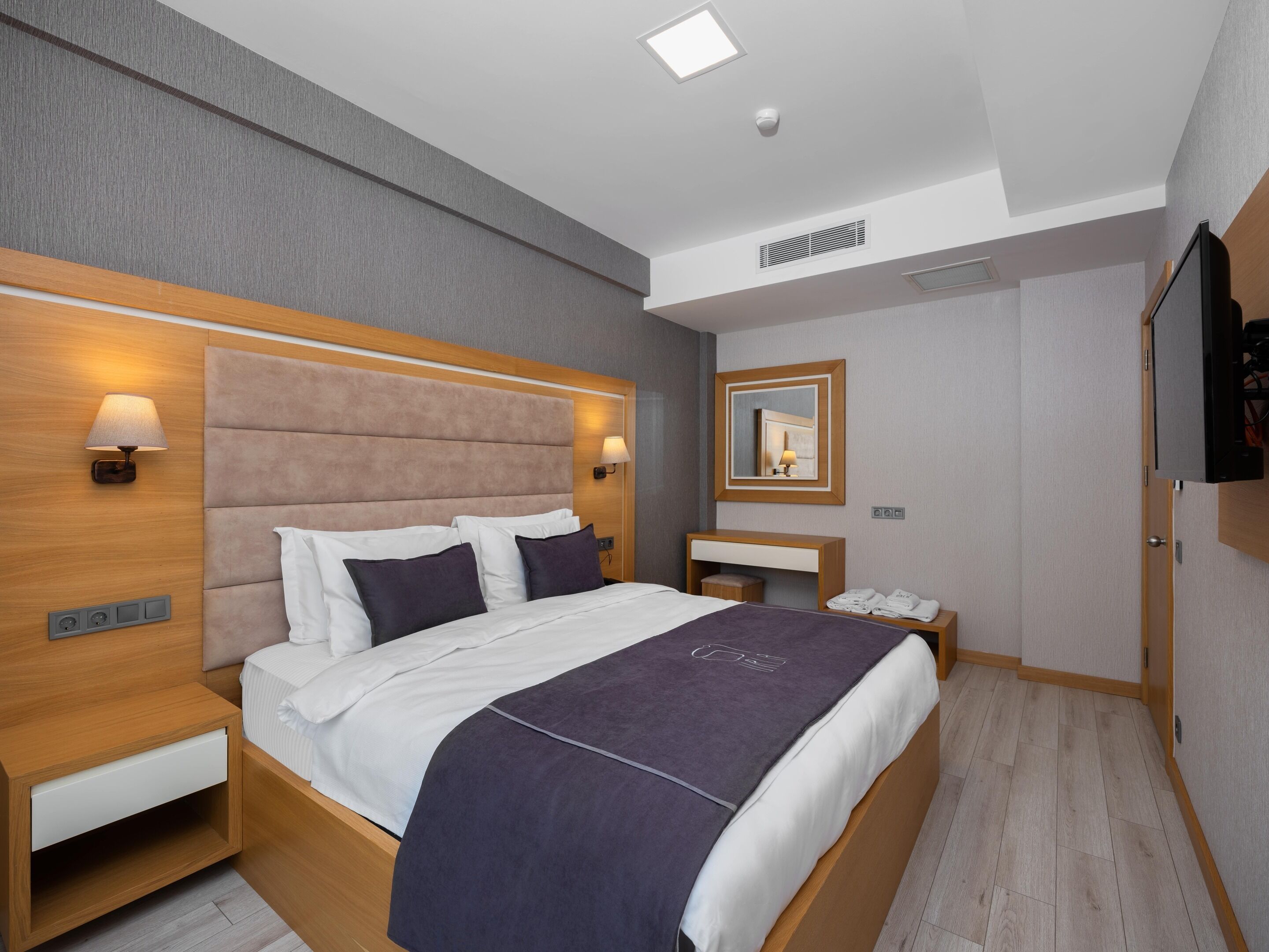 Een moderne hotelkamer met een groot bed, nachtkastjes, een bureau, een spiegel en een televisie.