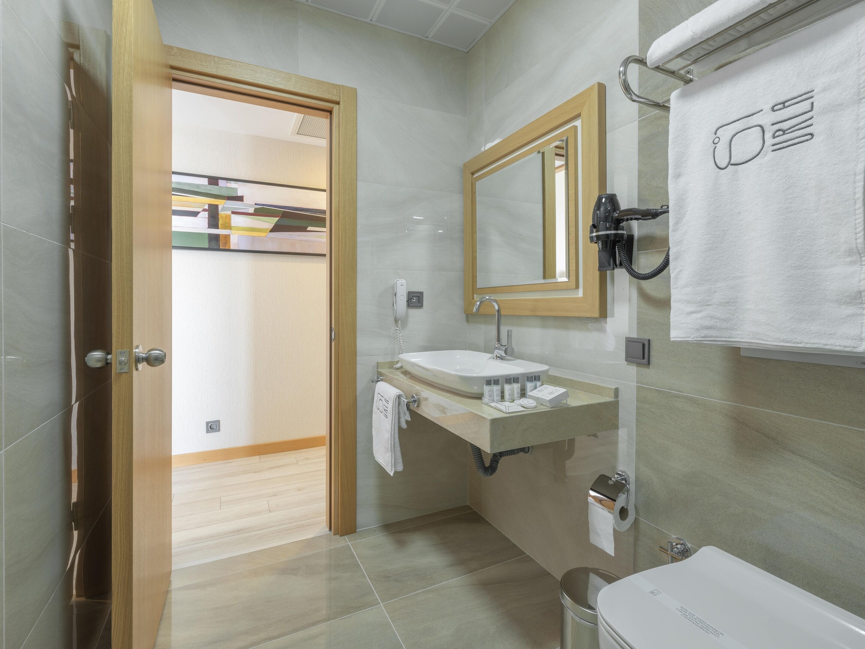 Un baño moderno con puerta de madera, un lavamanos con espejo y una toalla colgada en la pared.