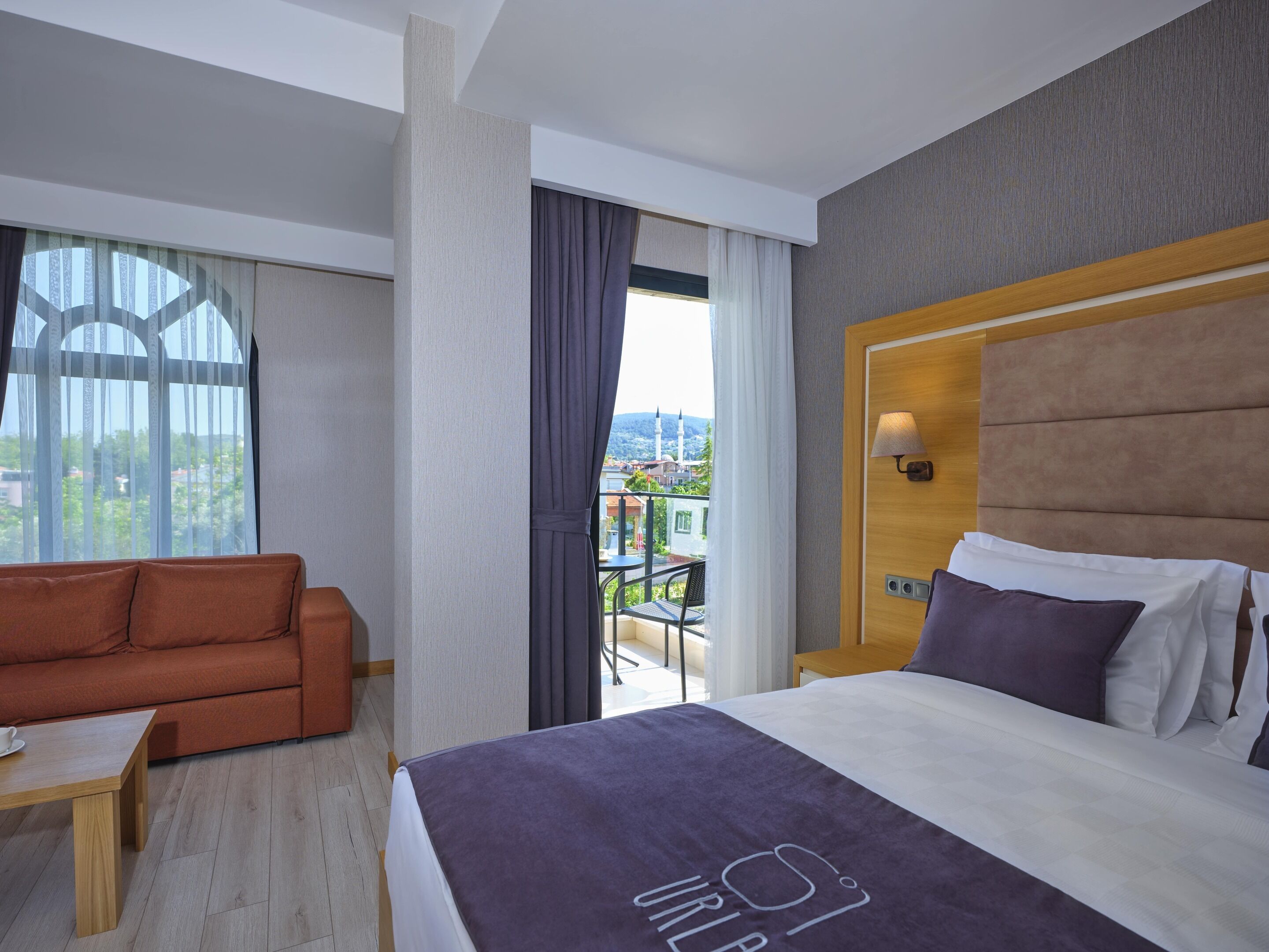 Une chambre d’hôtel comprenant un lit, un canapé, une table et un balcon offrant une vue sur des immeubles et une mosquée.