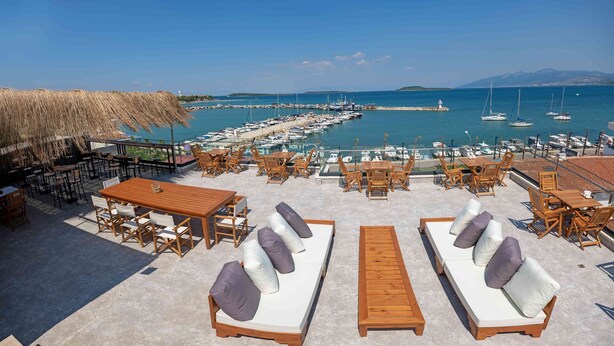 A seaside patio with wooden furniture, a thatched roof, and a view of a marina with boats. - Ma-Si Urla Hotel (Urla)