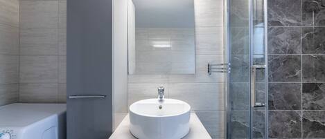 A modern bathroom with a white sink, a mirror, and a shower area with dark tiles.