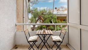 Un balcon avec une table en bois et deux chaises, une balustrade blanche et une vue sur des immeubles et des arbres.