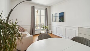Ett modernt rum med en vit soffa, ett matbord och ett stort fönster med gardiner.