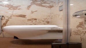 A modern bathroom with a white toilet, a shower, and a marble wall. - MeroStay 107 Hotel Bhairav Ananda  (Kathmandu)