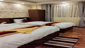 A hotel room with two beds, a wooden floor, a stone wall, and a large window with curtains. - MeroStay 107 Hotel Bhairav Ananda  (Kathmandu)