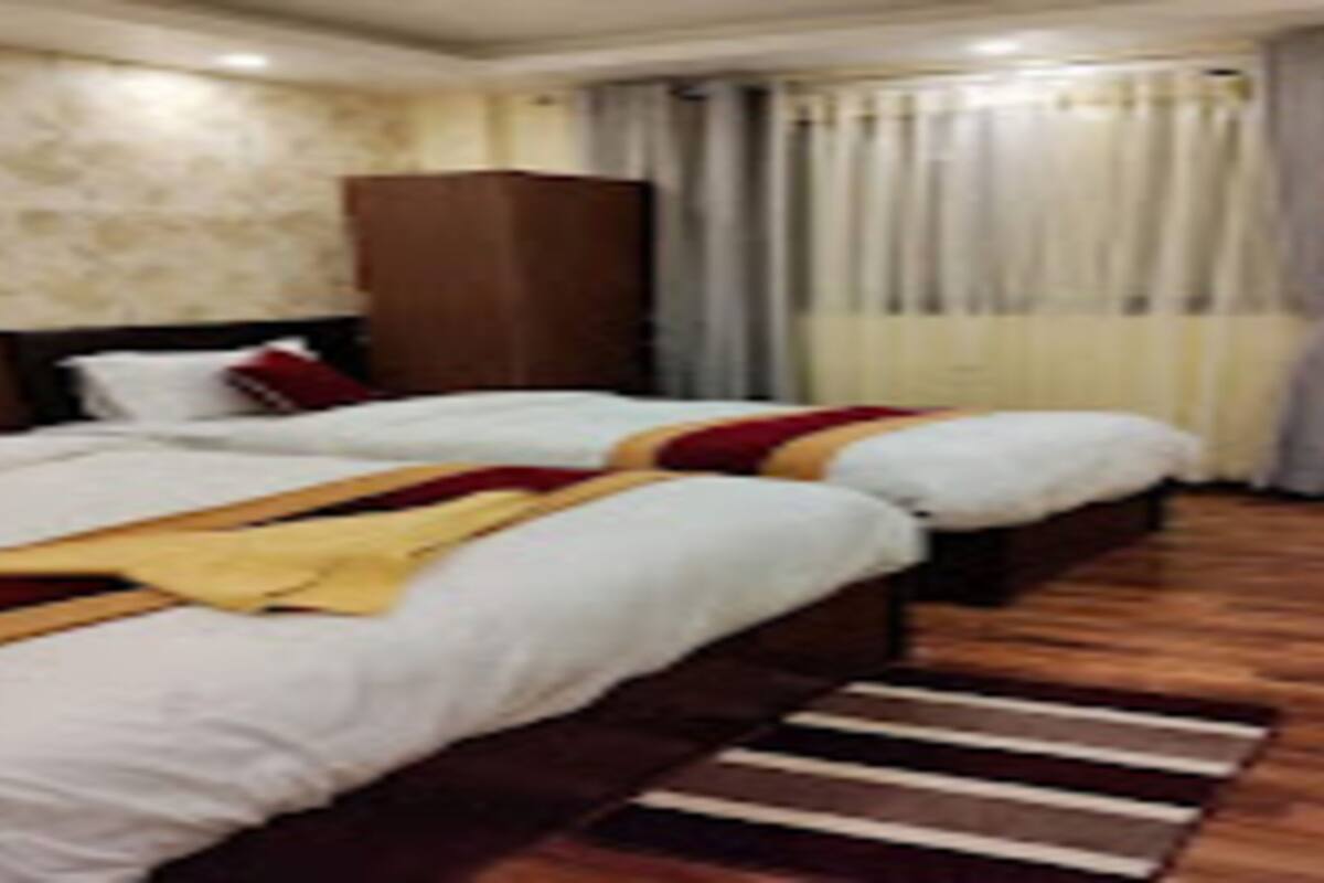 A hotel room with two beds, a wooden floor, a stone wall, and a large window with curtains.
