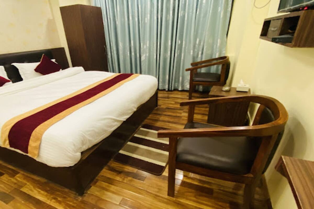 A hotel room with a large bed, a wooden chair, a small table, and a TV mounted on the wall.
