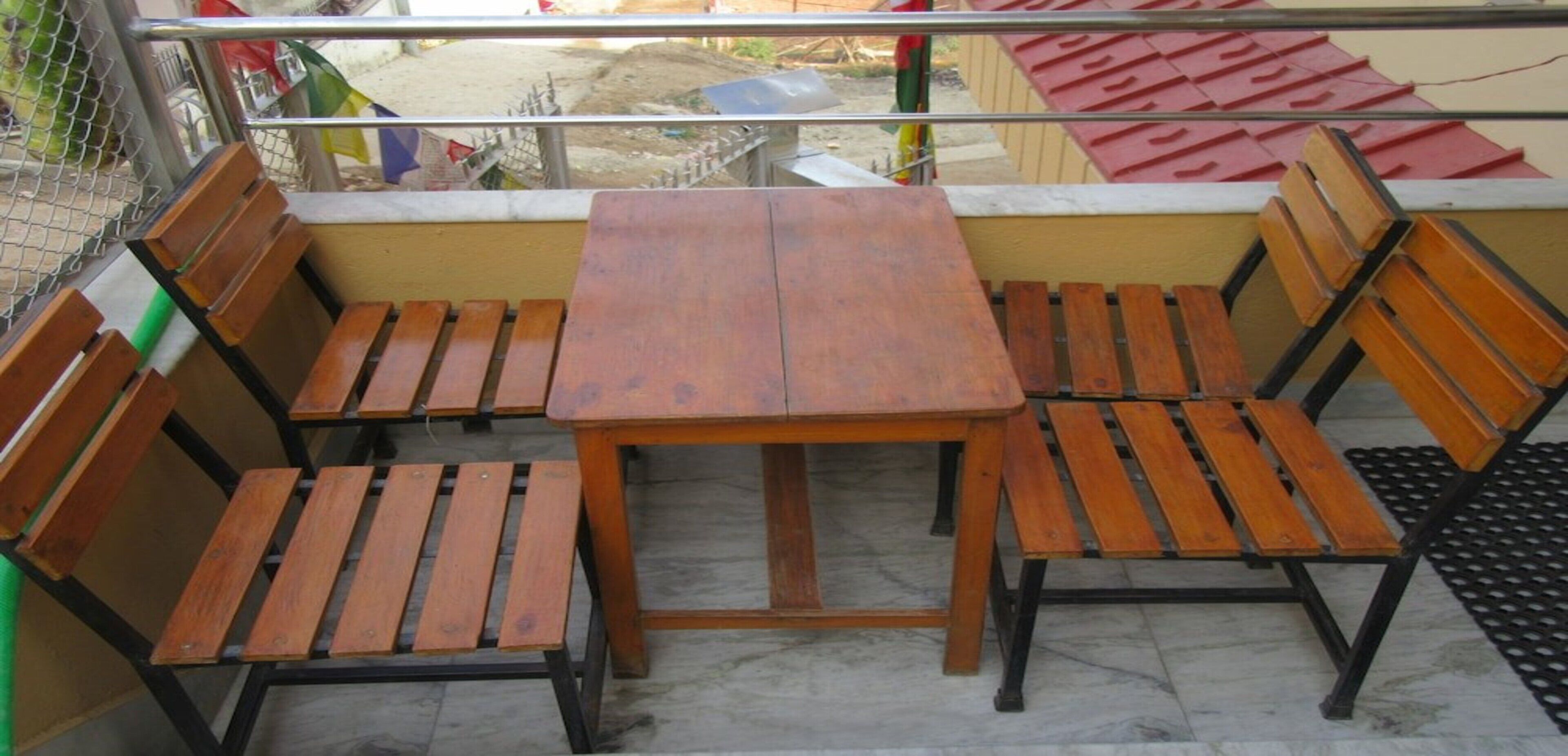 Een houten tafel en vier stoelen op een balkon met een metalen leuning.