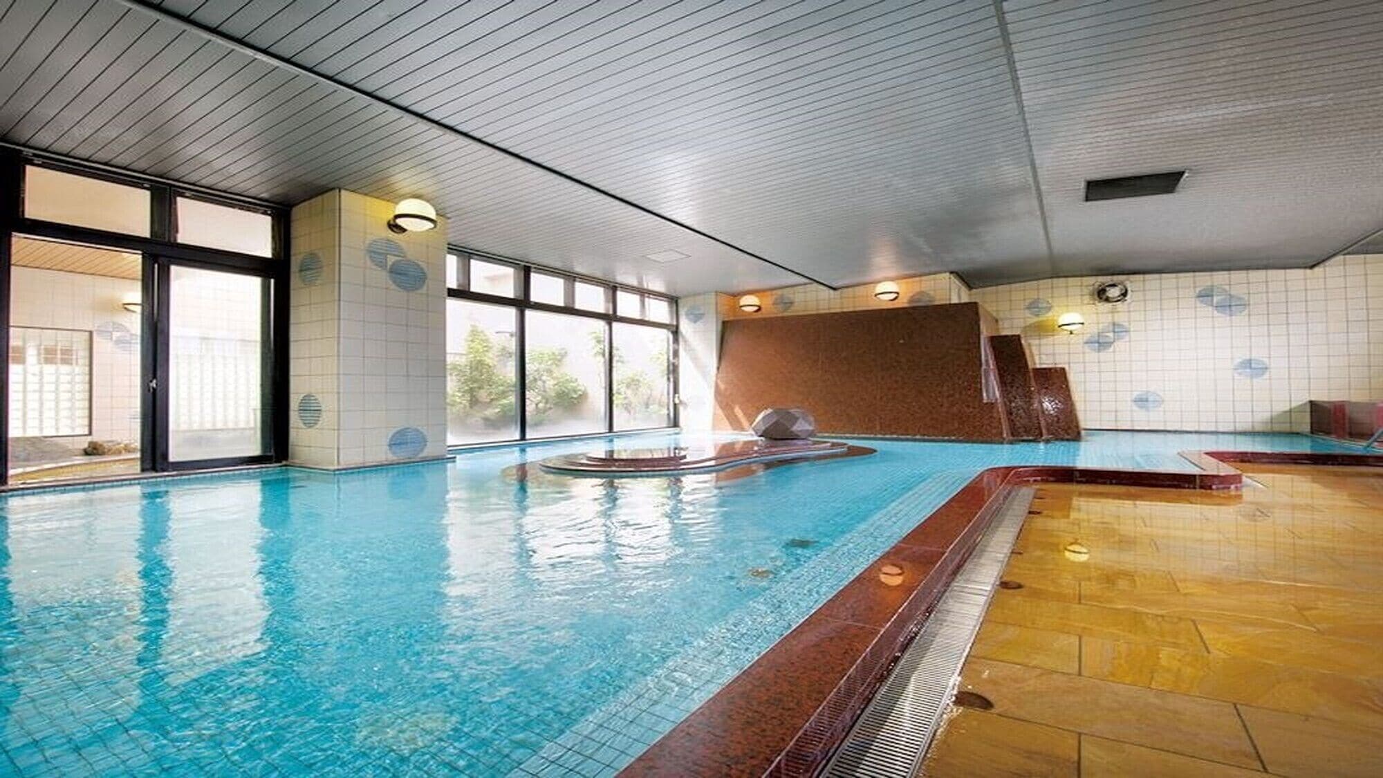 An indoor swimming pool with clear water, tiled walls, and a wooden floor.