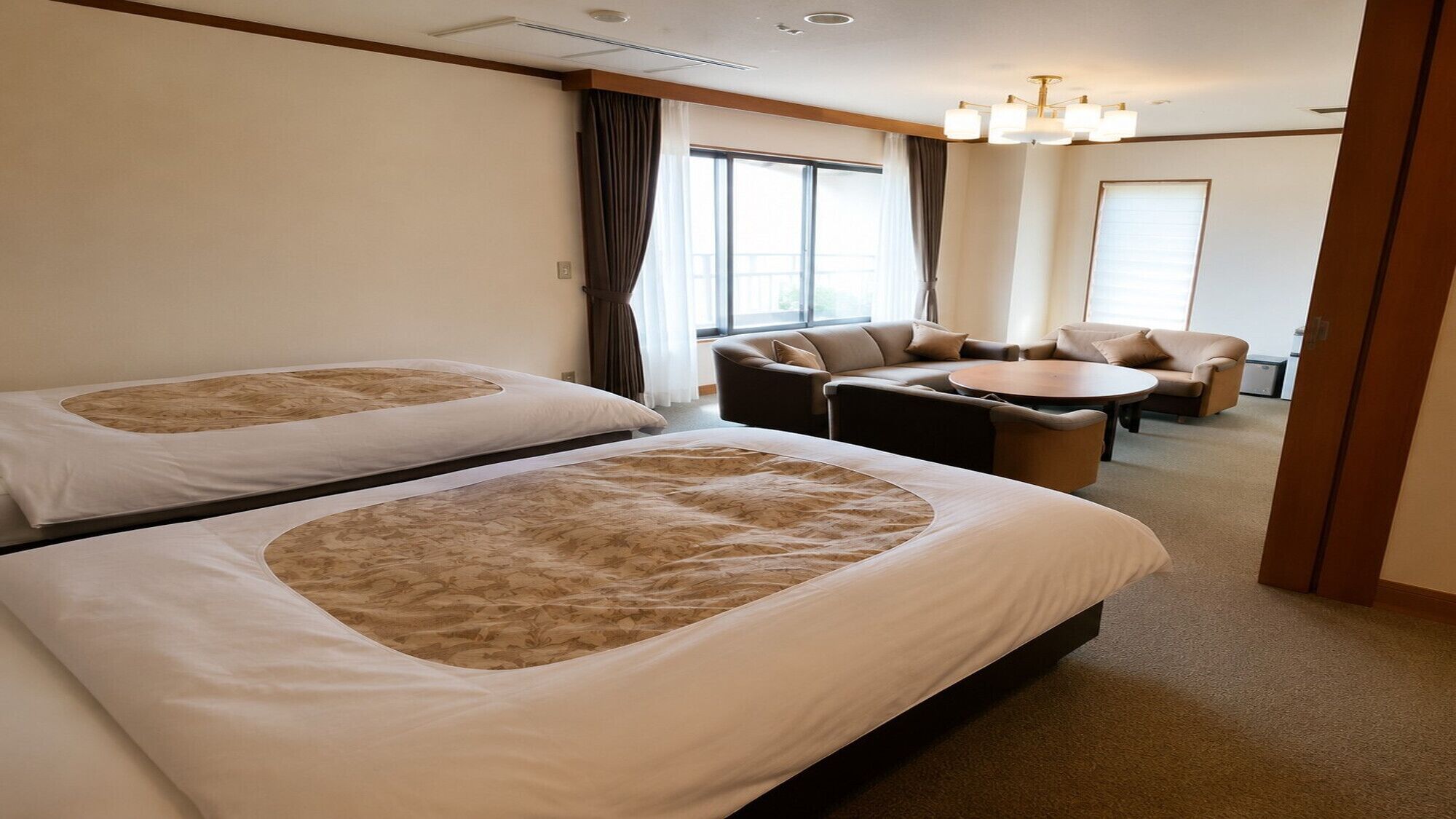 A hotel room with two beds, a sofa, a small table, and a view of the outdoors.