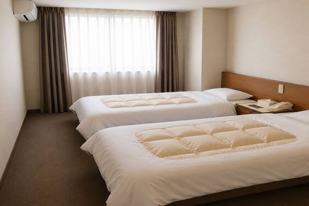 A hotel room with two beds, a bedside table with a phone, and a window with curtains.