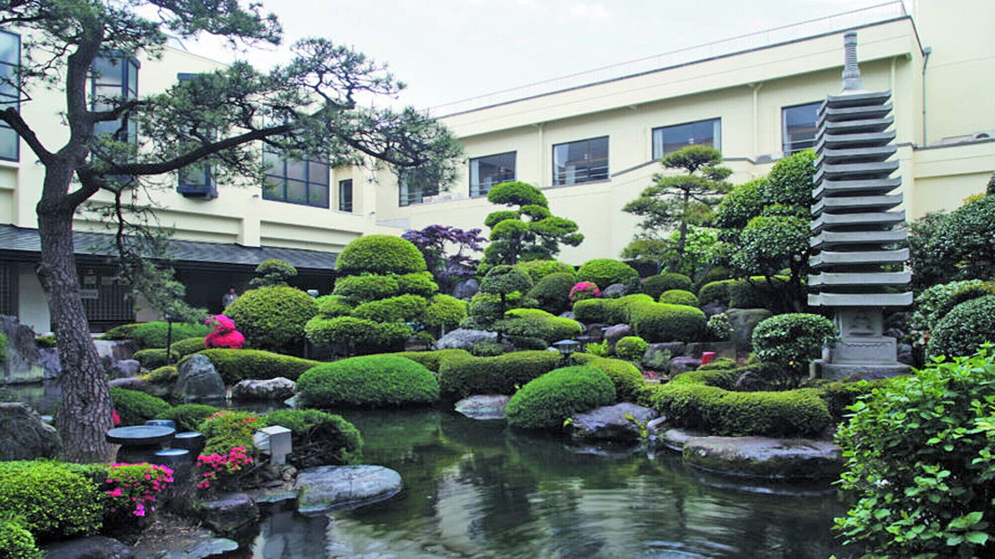 A traditional Japanese garden with a pond, rocks, and well-manicured trees.