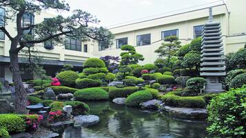 A traditional Japanese garden with a pond, rocks, and well-manicured trees.