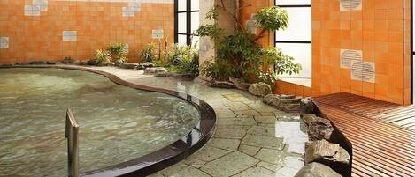 An indoor swimming pool with a wooden deck, surrounded by plants and stone tiles.