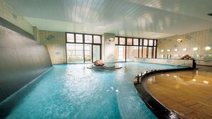 An indoor swimming pool with a central water feature, large windows, and a wooden floor. - LiVEMAX RESORT Isawa Onsen (Fuefuki)