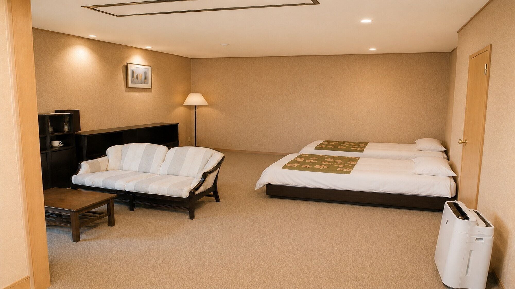 Habitación de hotel con sofá, dos camas, escritorio, lámpara y un cesto de basura.