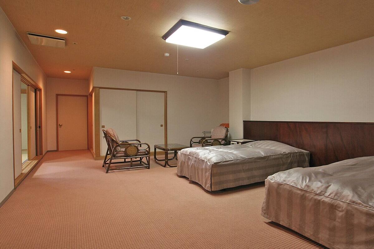 A hotel room with two beds, a chair, a small table, and a wardrobe.
