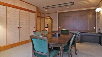Une salle de conférence avec une table en bois, des chaises recouvertes d’un tissu vert, une petite table avec un téléphone et un grand miroir au mur.
