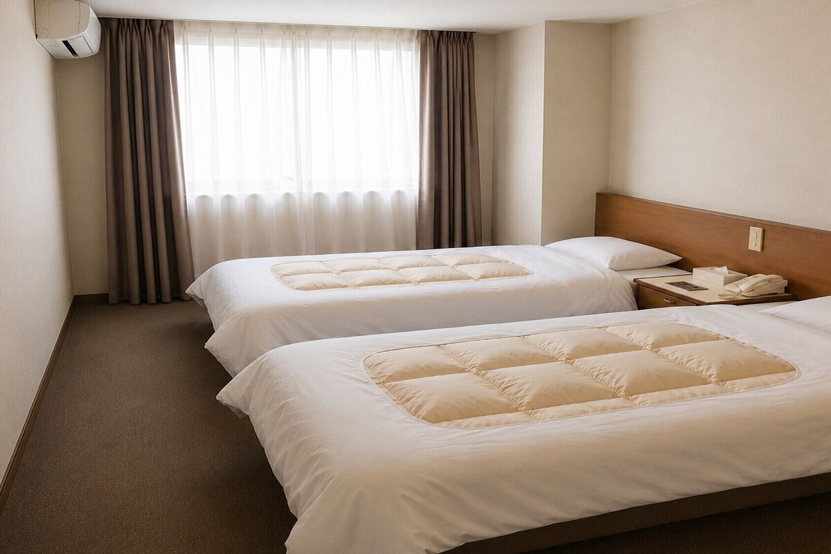 A hotel room with two beds, a bedside table with a phone, and a window with curtains.