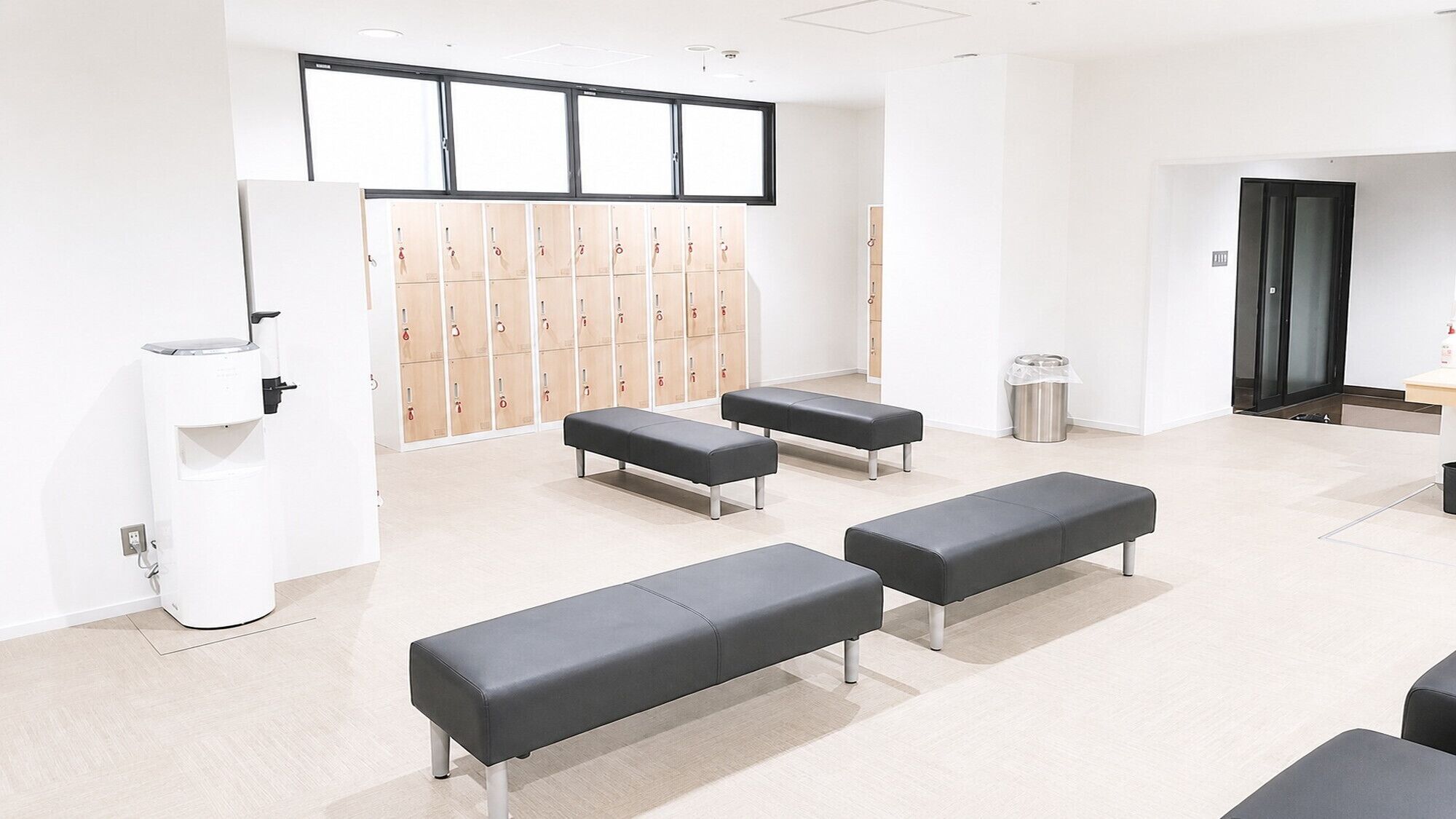 A clean, modern waiting area with benches, a trash bin, and lockers in the background.