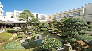 A traditional Japanese garden with a pond, rocks, and neatly trimmed bushes. - LiVEMAX RESORT Isawa Onsen (Fuefuki)