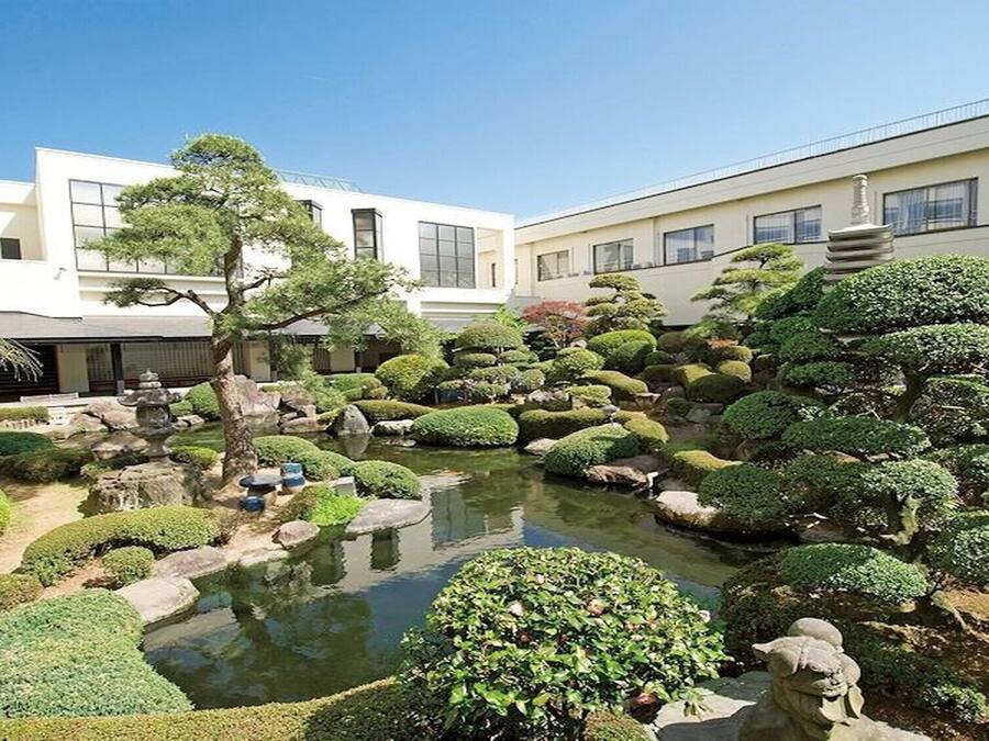 A traditional Japanese garden with a pond, rocks, and neatly trimmed bushes.