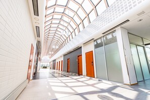 Een moderne hotelgang met een hoge plafond en dakramen, met meerdere deuren en een glazen wand.