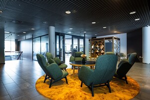 Un vestíbulo moderno con sillas tapizadas de verde alrededor de una mesa central, ventanas amplias y un techo con diseño.