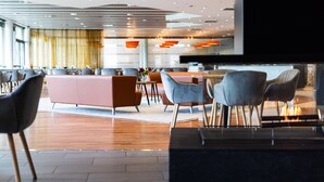 Un moderno vestíbulo de hotel con un área de estar central, un televisor y una cocina al fondo.