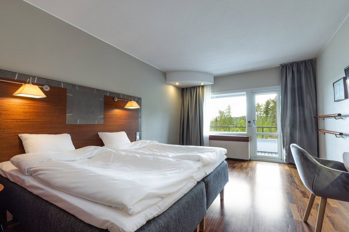 A modern hotel room with a large bed, a desk, and a view of the outdoors.