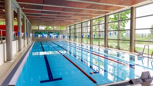 Una piscina interior larga con carriles bien definidos, ventanas amplias y un techo alto con diseño de madera.