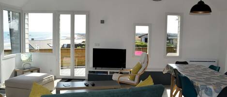 Un salón amplio con televisor grande, asientos cómodos y vista a la playa.
