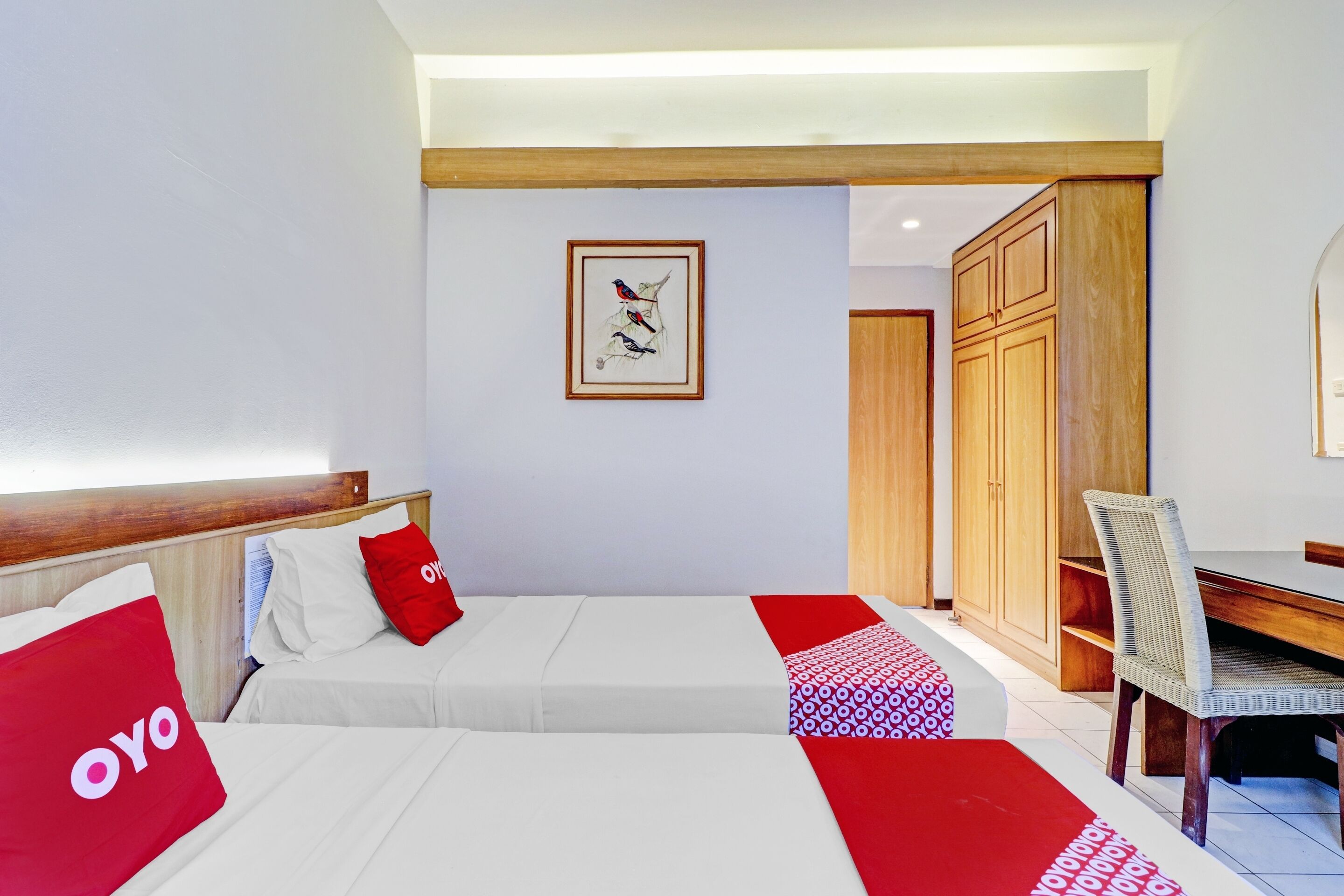 A hotel room with two beds, a wooden headboard, a framed artwork on the wall, and a dining area with a chair and table.