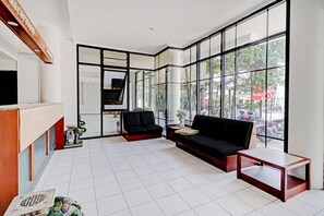 Et moderne receptionsområde med en sort sofa, et træreceptionistskrivebord og store vinduer med udsigt til gaden.
