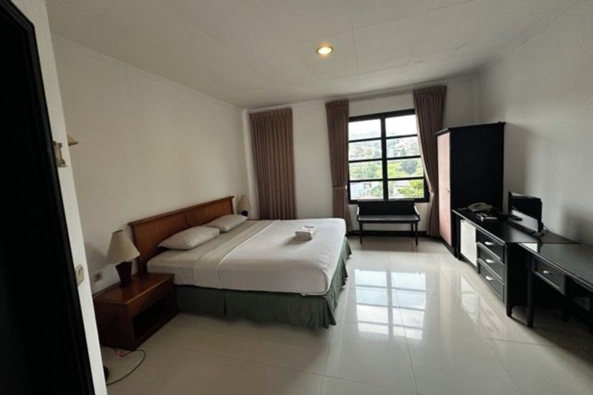 Una habitación de hotel con cama, escritorio, televisor y ventana con cortinas.