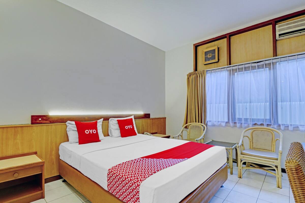 Habitación de hotel con cama, mesita de noche, una silla y ventana con cortinas.