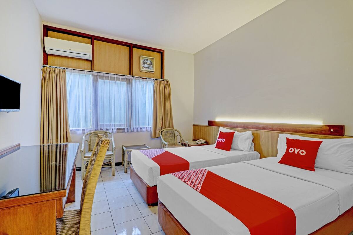 Habitación de hotel con dos camas, un escritorio, una silla, un televisor y una ventana con cortinas.